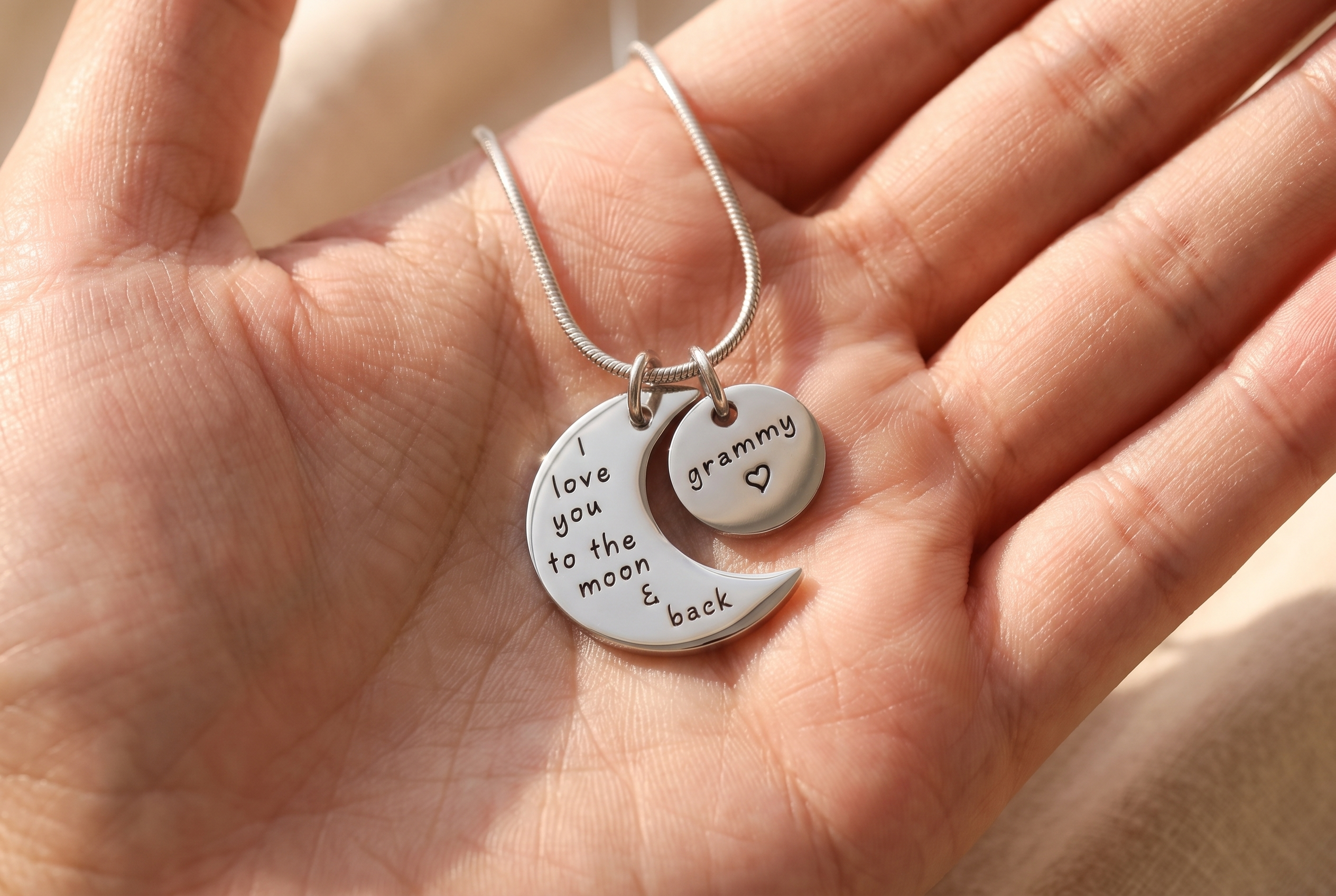 Engraved name disc and crescent pendant held in a mother's palm