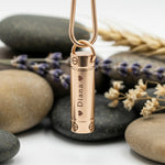 Rose gold Belle Fever Cylinder Cremation Necklace resting on stones — a beautifully handcrafted piece to cherish and remember loved ones forever