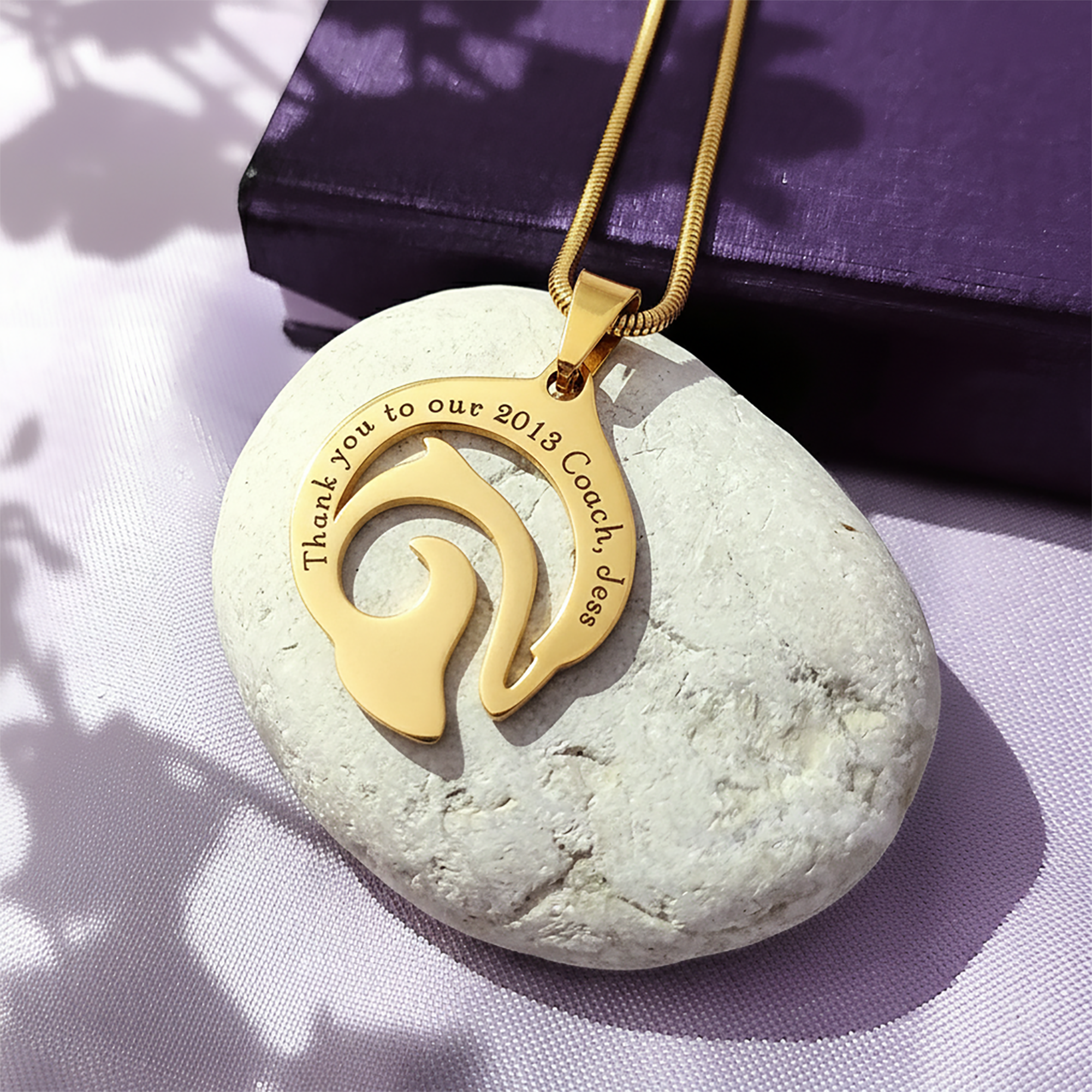 Custom engraved dolphin necklace in gold on purple background, meaningful freedom and resilience jewelry by belle fever.