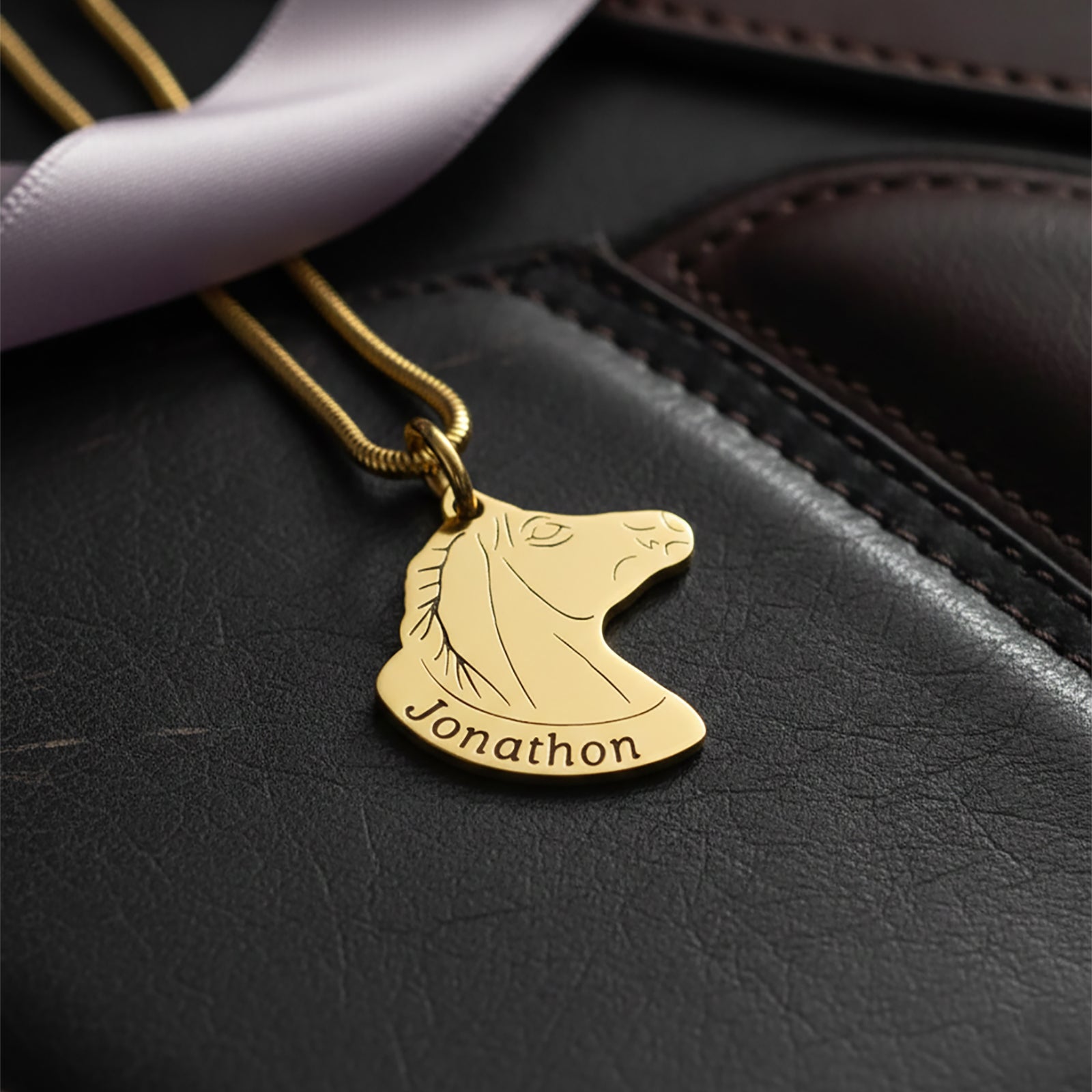 Belle Fever Horse Head Necklace with Custom Name in gold resting on black leather background, custom engraved horse pendant necklace, luxury personalised equestrian jewellery gift.