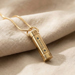 Gold cylinder cremation necklace with urn pendant displayed on neutral background