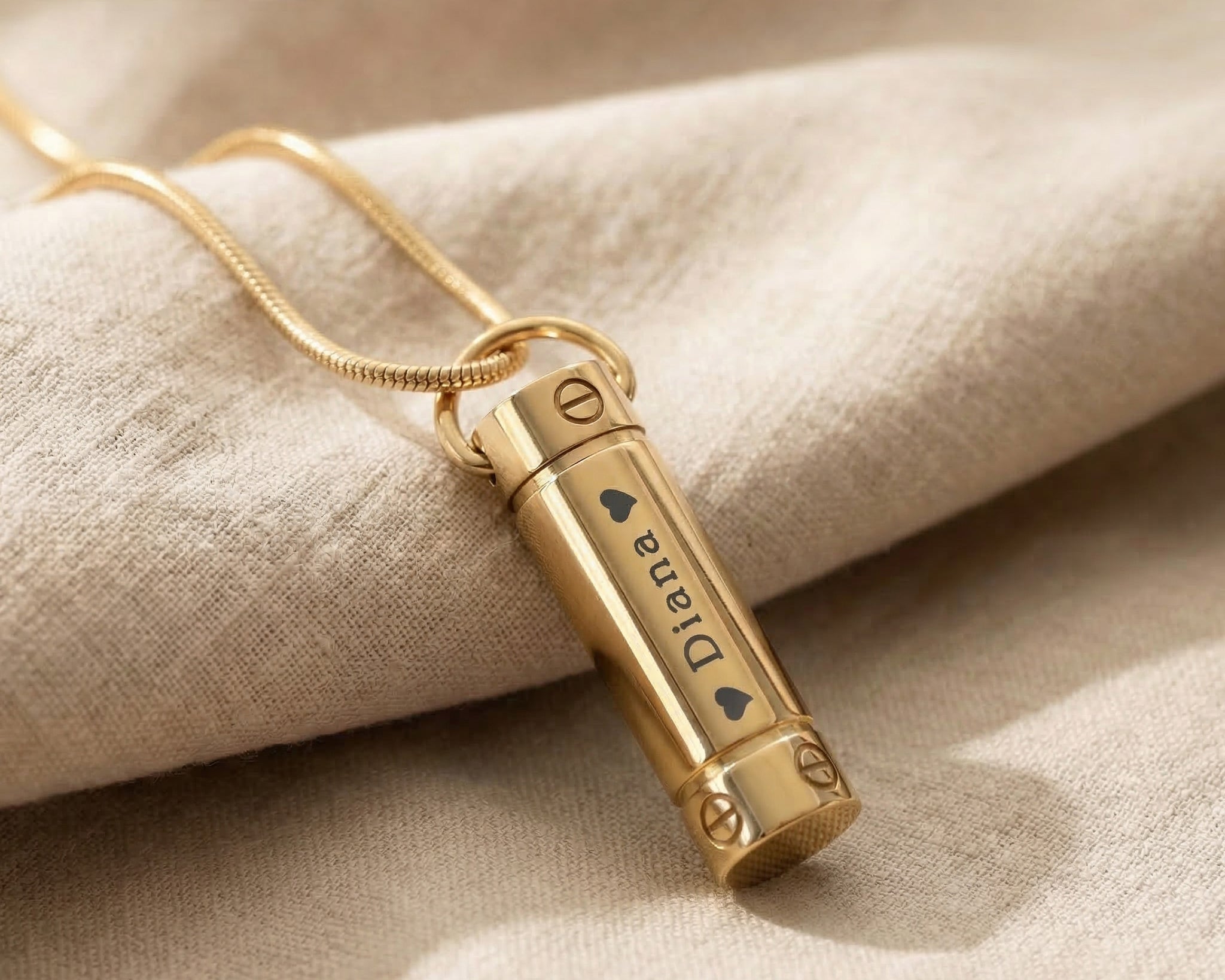 Gold cylinder cremation necklace with urn pendant displayed on neutral background