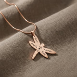 Dragonfly Necklace with Custom Engraved Names by Belle Fever in rose gold on textured taupe fabric, symbolic strength and transformation gift for women.