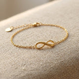 Gold infinity bracelet with delicate chain and infinity symbol displayed on neutral fabric background
