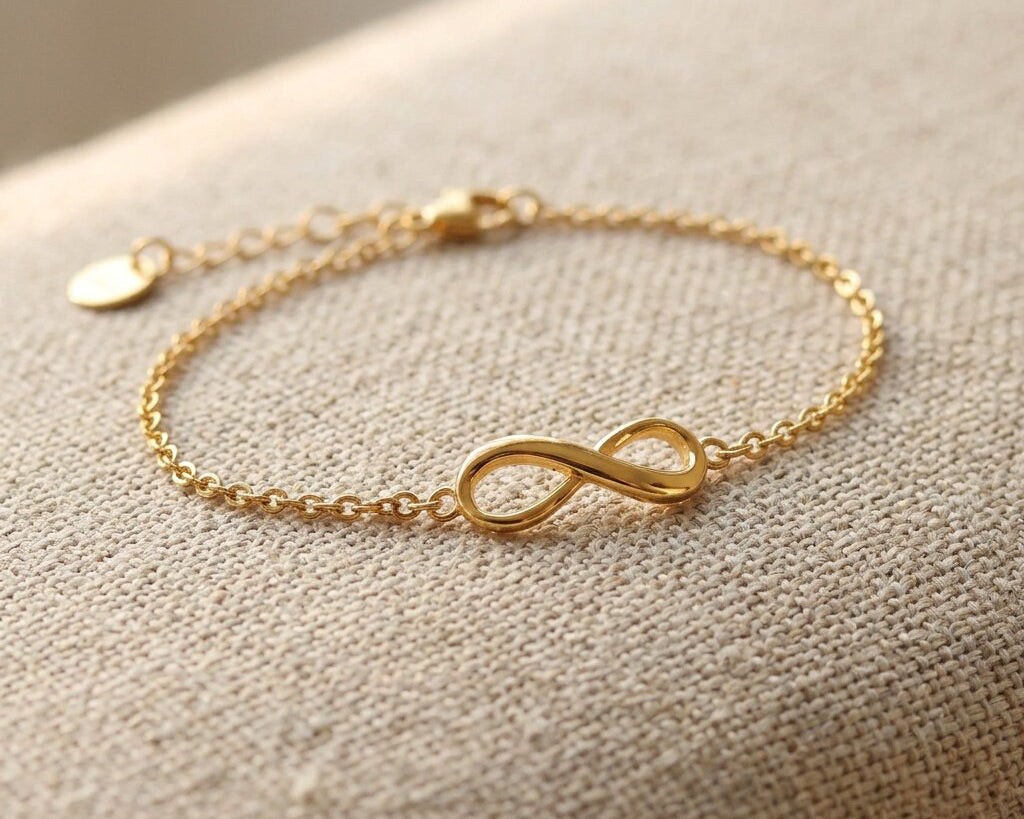 Gold infinity bracelet with delicate chain and infinity symbol displayed on neutral fabric background