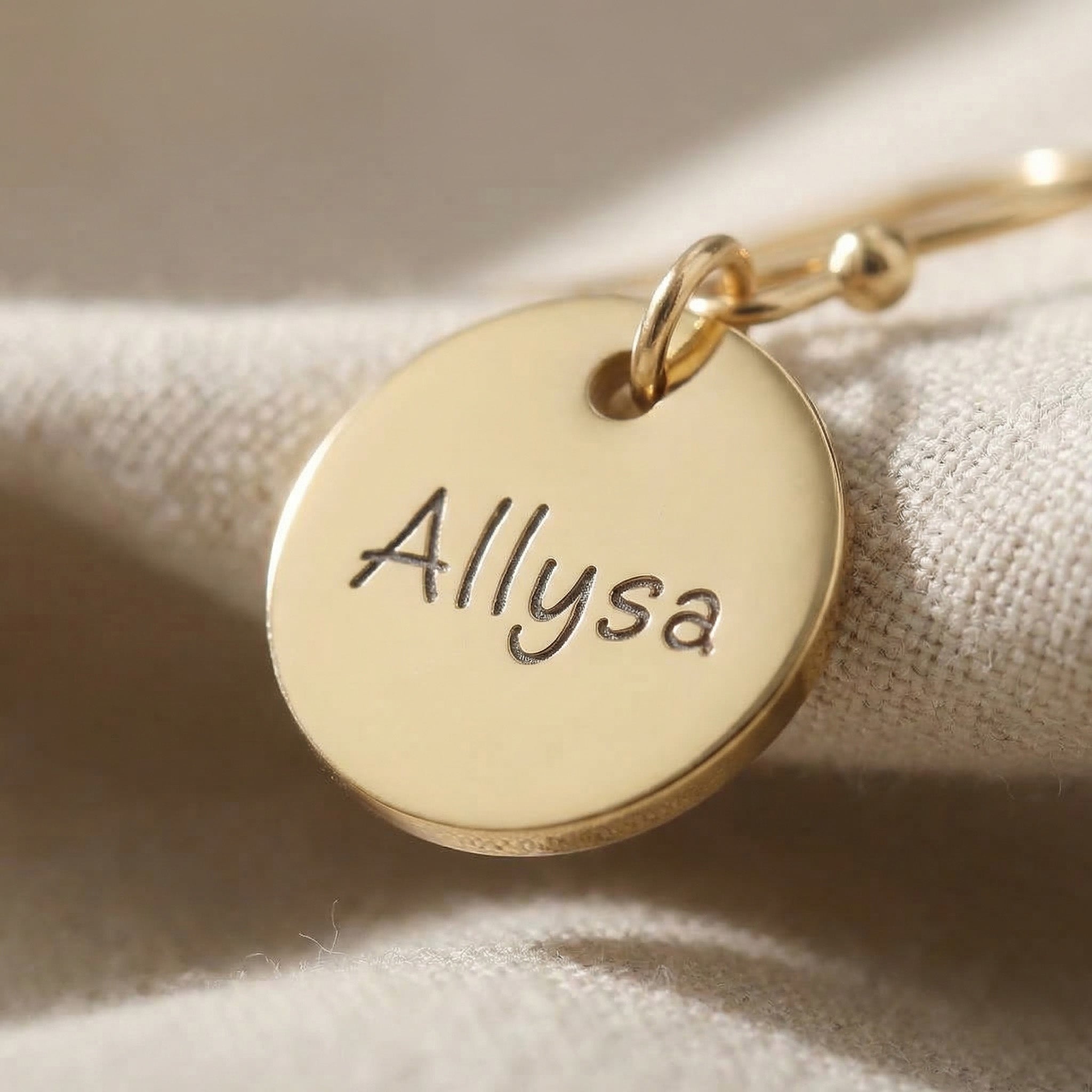 Close up of personalised earrings showing engraved name detail on round disc