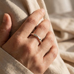 Woman wearing wave band ring, elegant minimalist jewellery with flowing curved band design for everyday wear